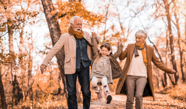 Grandparents swinging their granddaughter while walking through autumn woods